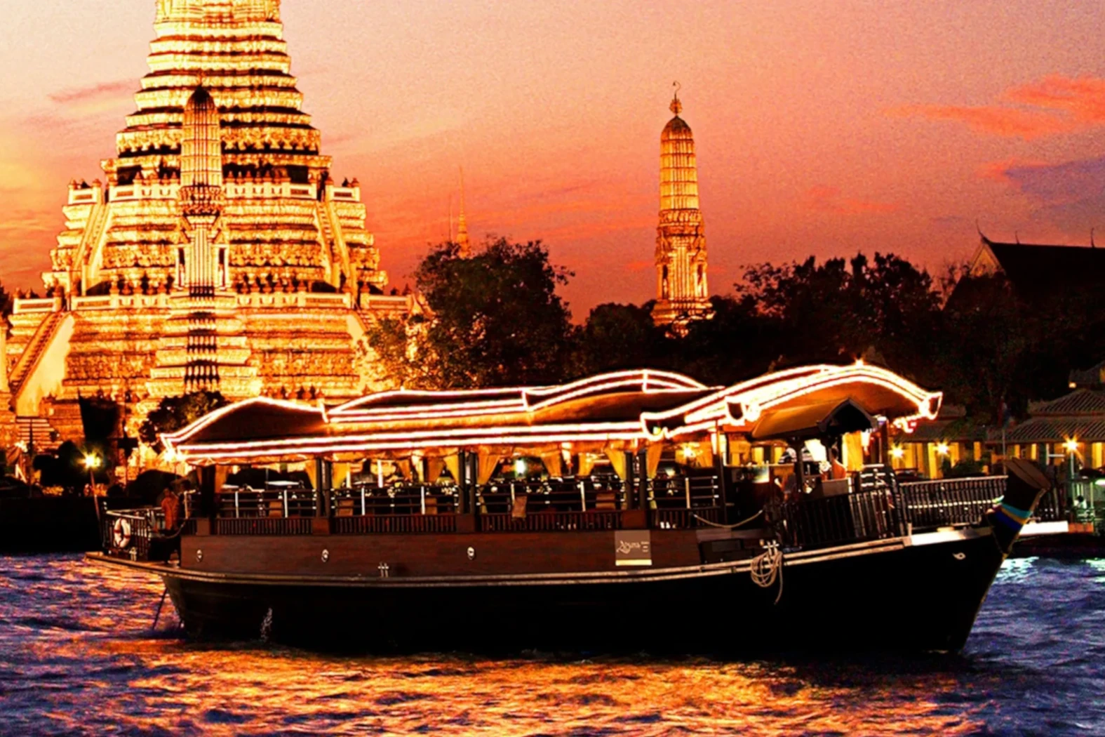 Night view of a temple and the boat of Apsara during a dinner cruise on the river in Bangkok.