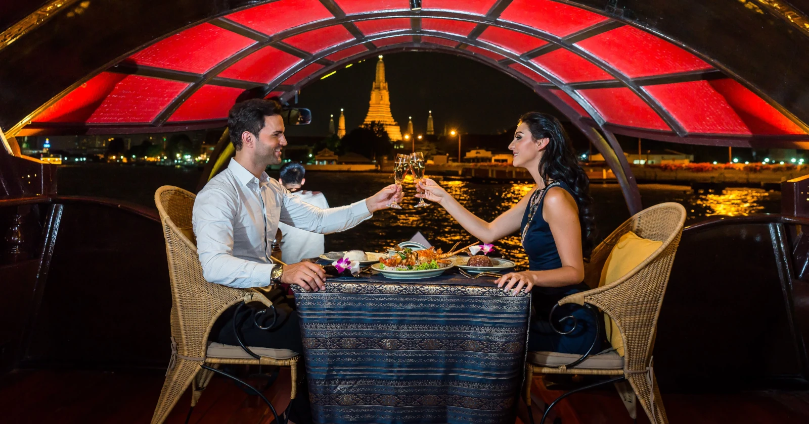 Romantic private dinner aboard a boat during a night dinner cruise in Bangkok with the Wat Arun in the background.