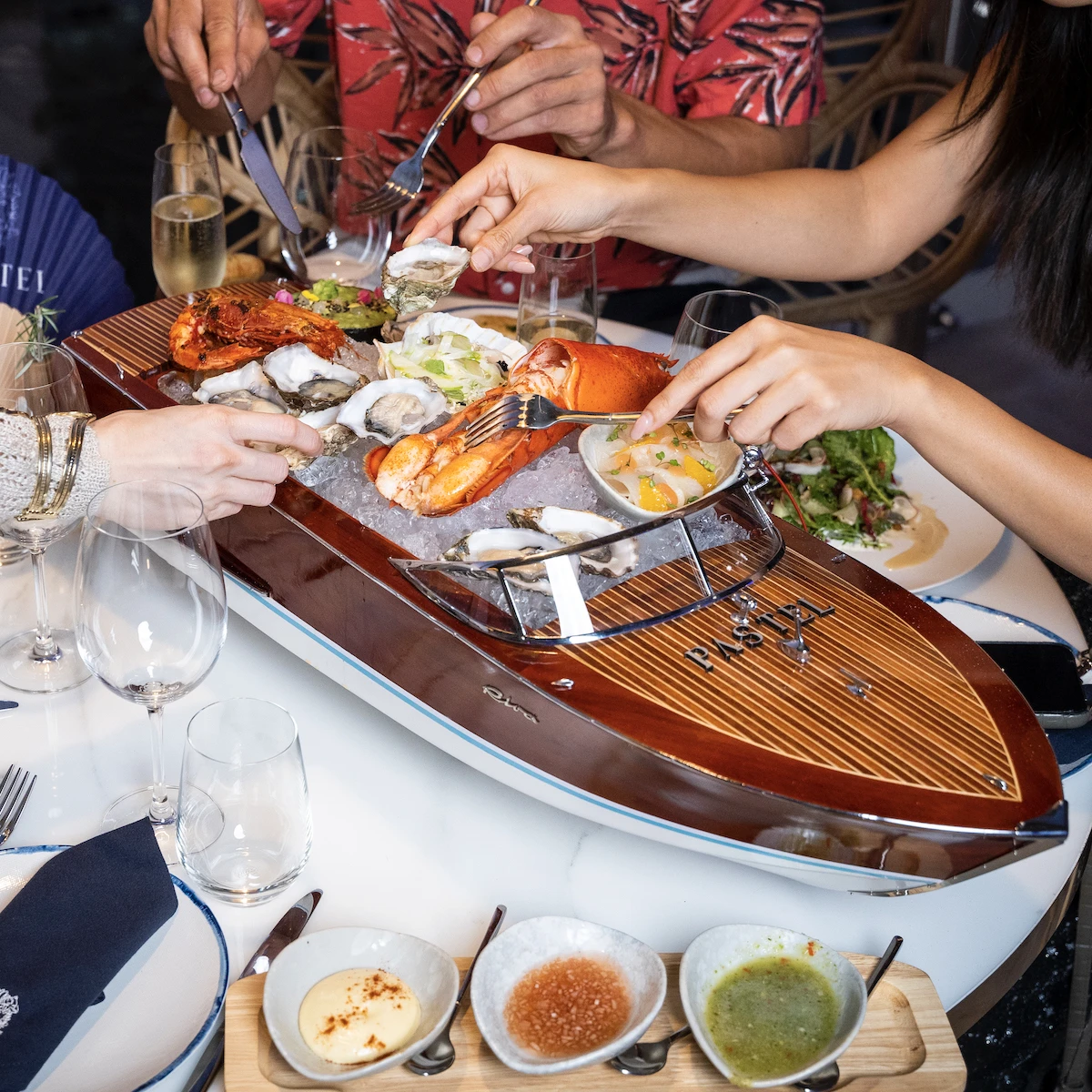 People grabbing food from Pastel Bangkok seafood yacht with knives and forks.
