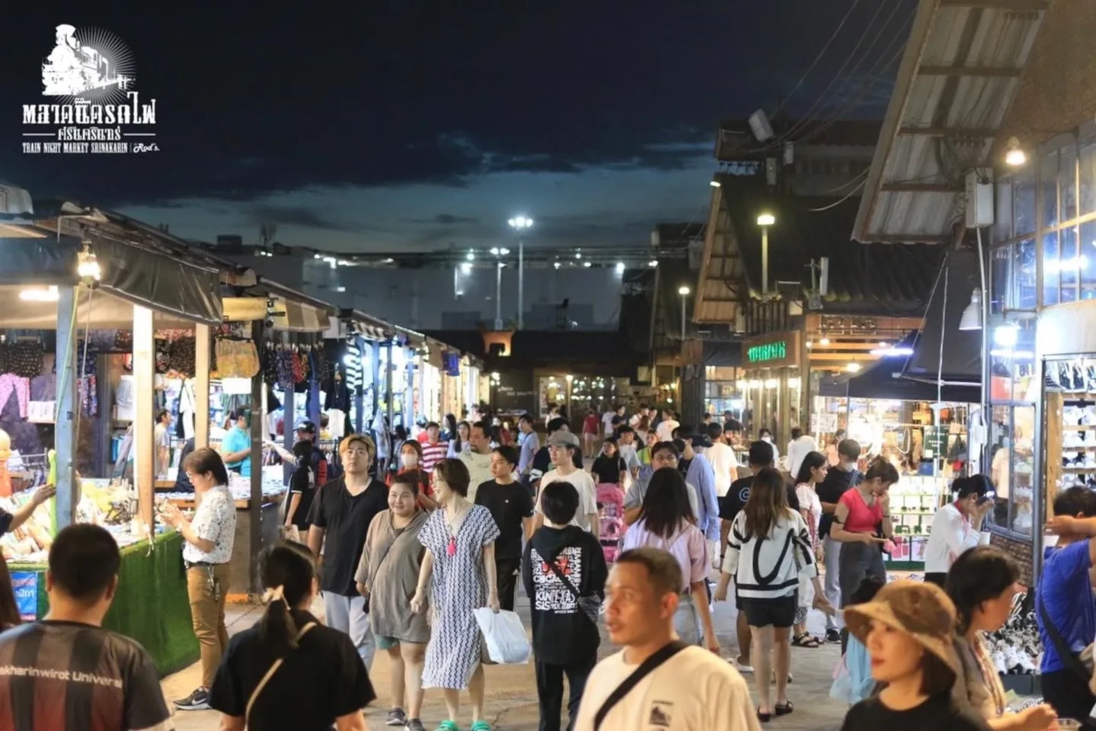 People walking at the Srinagarindra Train Market at night in Bangkok.