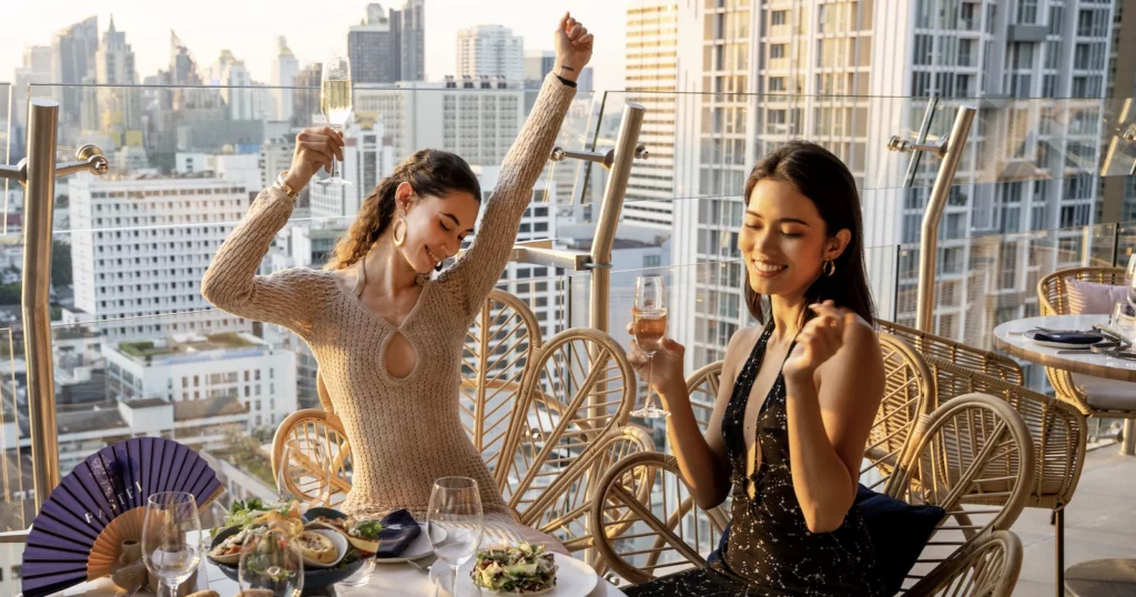 A Thai Instagram models smiling and dancing at the Pastel rooftop bar with sunset behind her