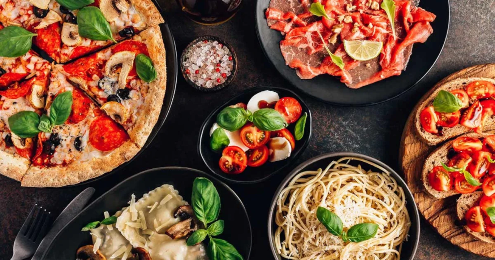 Picture of traditional Italian food on a table with pizza, pasta and mozzarella.